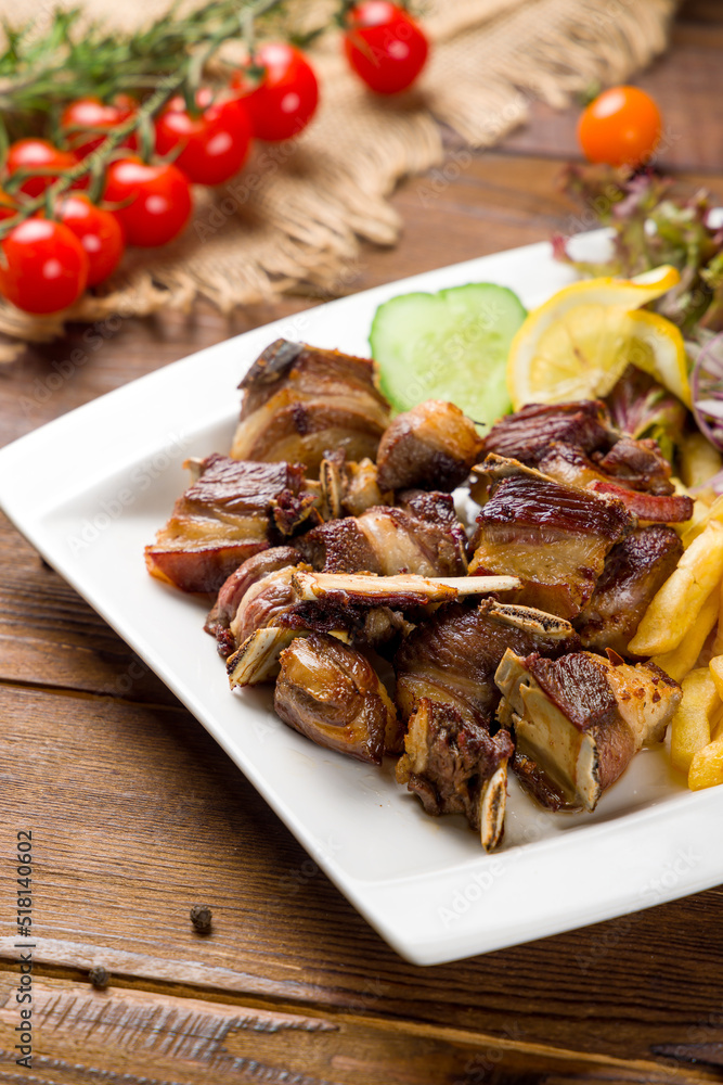 Kebab from lamb ribs with french fries on white plate on wooden table Kebab from lamb ribs with french fries on white plate on wooden table