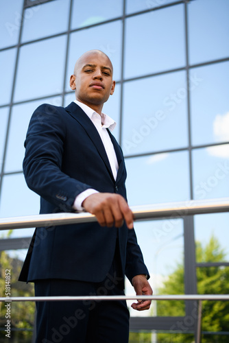 Low angle view of african american manager in suit looking at camera near railing outdoors 