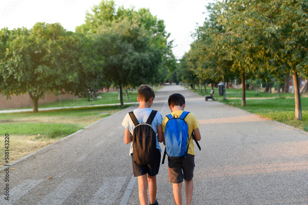 Two children with backpacks on their backs stroll through a park. Concept of back to school Two children with backpacks on their backs stroll through a park. Concept of back to school