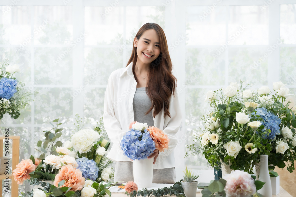 Young Asian woman stand at desk at home make beautiful floral compositions for sale. Florist talking and making beautiful bouquet of flower.