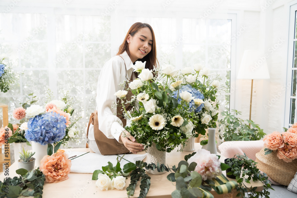 Young Asian woman stand at desk at home make beautiful floral compositions for sale. Florist talking and making beautiful bouquet of flower.
