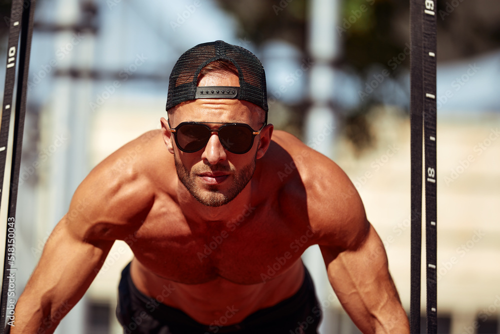 Fototapeta premium Young and handsome man is doing some push-ups. He is using loops for that