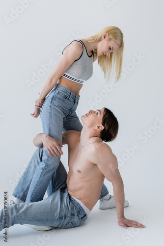 Side view of blonde woman in top looking at sexy boyfriend in jeans on grey background.