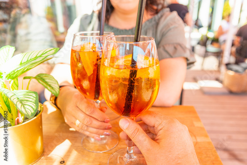 Woman and man making a celebratory toast with aperol spritz orange alcoholic cocktails at outdoors cocktail bar.Close up.