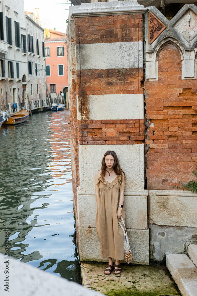 Young woman in dress looking at camera near old building in Venice.