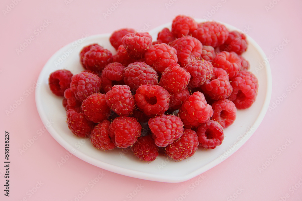 large ripe raspberries in a white plate in the shape of a heart on a pink background large ripe raspberries in a white plate in the shape of a heart on a pink background