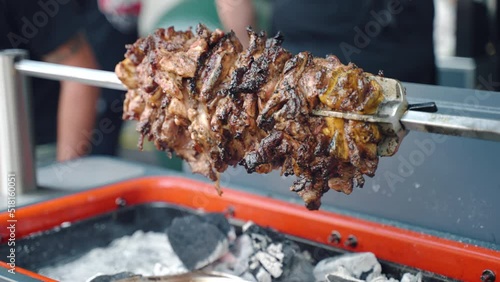 Barbecue festival outdoor, fat pork roasting on fire, juicy meat pieces rotating on skewer above the hot charcoals and rising smoke. Meat spit gilling in smoker, cookout picnic dinner photo