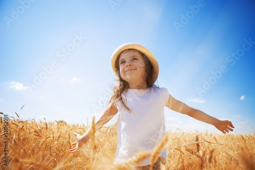 Happy girl walking in golden wheat, enjoying the life in the field. Nature beauty, blue sky and field of wheat. Family outdoor lifestyle. Freedom concept. Cute little girl in summer field © Dmytro Sunagatov