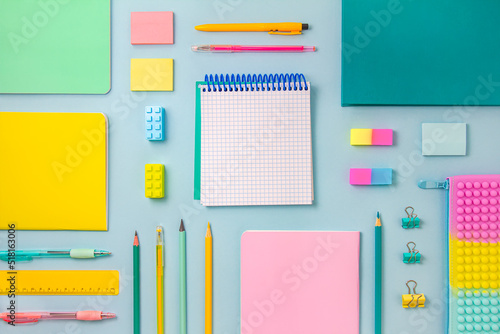 The concept of back to school. Pastel-colored stationery and an inscription pad are arranged in order on a blue background. Top view, flat lay, copy space