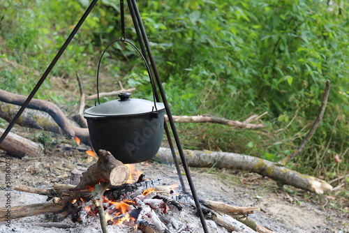 cooking delicious tasty food outdoors on fire in iron pot in summer in good weather with wood from forest