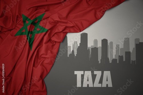 abstract silhouette of the city with text Taza near waving colorful national flag of morocco on a gray background.