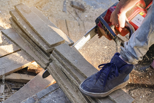 Cutting old wooden chipboards with electric chainsaw, splinters flying in air, closeup detail