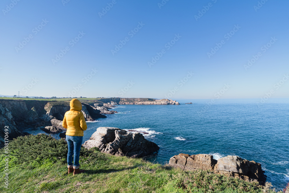 Coastal landscape and girl in yellow hooded coat looking at sea and walking. Copy space.