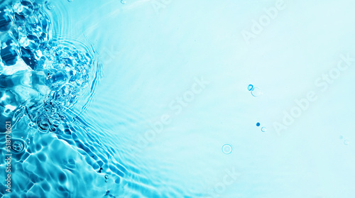 Blue liquid colored clear water surface texture with splashes bubbles. Water waves in sunlight background. Trendy summer nature banner. 
