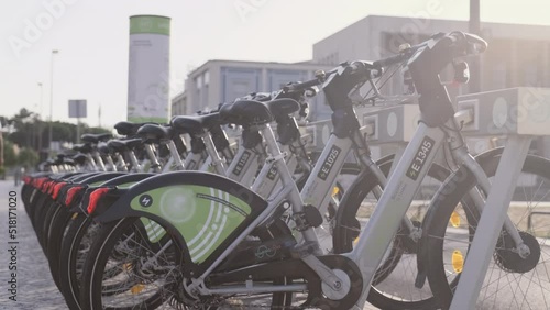 Bicycle rental service on city road. Public green transportation.  New bike sharing system along the streets of the city. Group of grey bikes ready to use. Portugal, Lisboa. July 16, 2022.