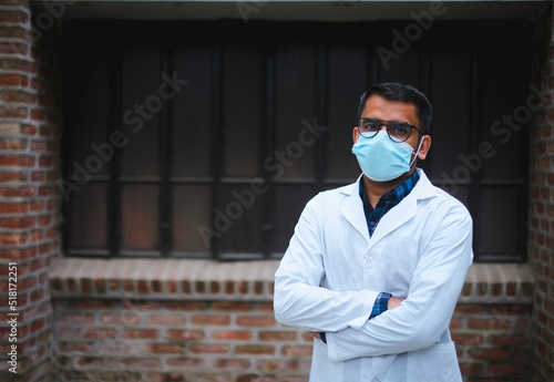 South asian young confident male doctor in white apron and face mask, Bangladeshi muslim medical student, protection from corona virus and flu viruses