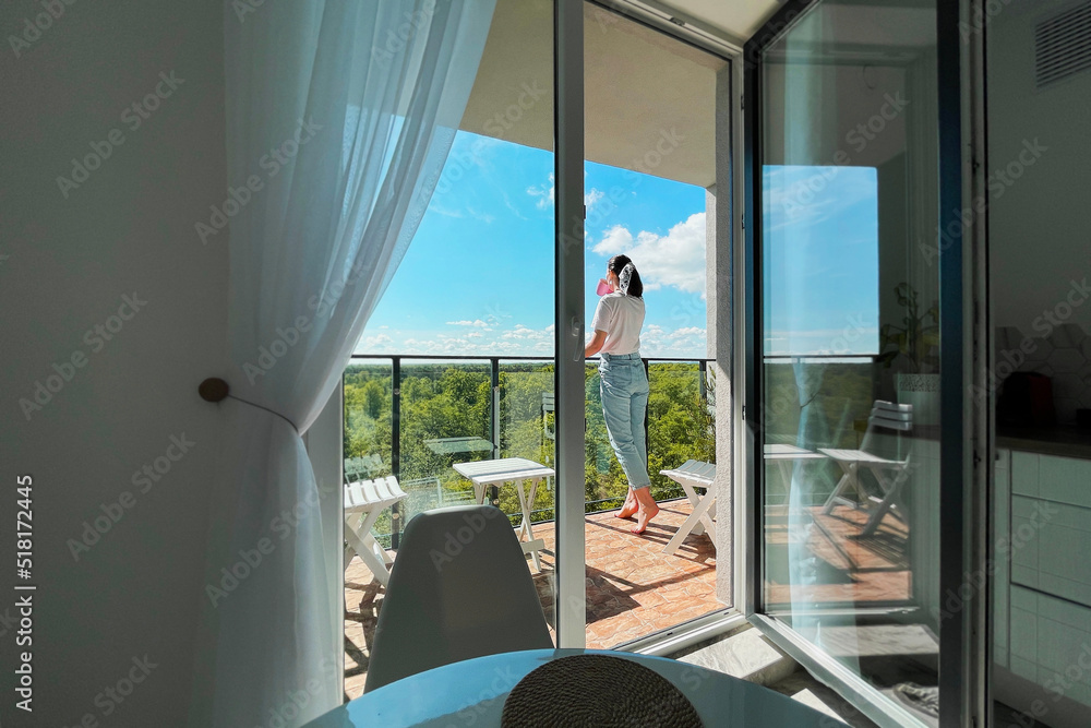 a girl with a mug on the balcony drinks morning tea and takes a break from the hustle and bustle of the city. Lifestyle. relaxing on the balcony with a view of the forest a girl with a mug on the balcony drinks morning tea and takes a break from the hustle and bustle of the city. Lifestyle. relaxing on the balcony with a view of the forest