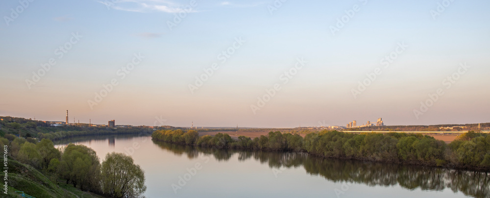 Fototapeta premium Evening landscape. Cloudy May day. Clouds are reflected in the lake. Peaceful landscape on the banks of the reservoir. Relax in nature.