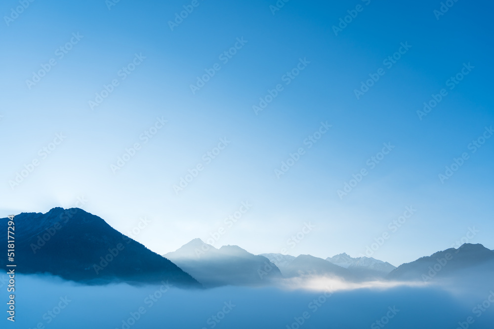 Blue moutains silhouette with fog in the valley. Beautiful fresh and bright morning in the alps.