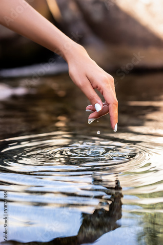 Detail of woman hand touching the surface of the water in the forest river