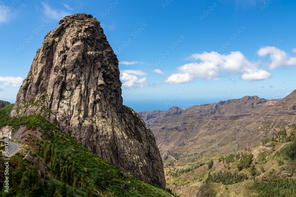 Fototapeta premium Scenic view on massive volcanic rock formation Roque de Agando in Garajonay National Park on La Gomera, Canary Islands, Spain, Europe. Lava cone of an old volcano. Hiking trail on sunny day in summer