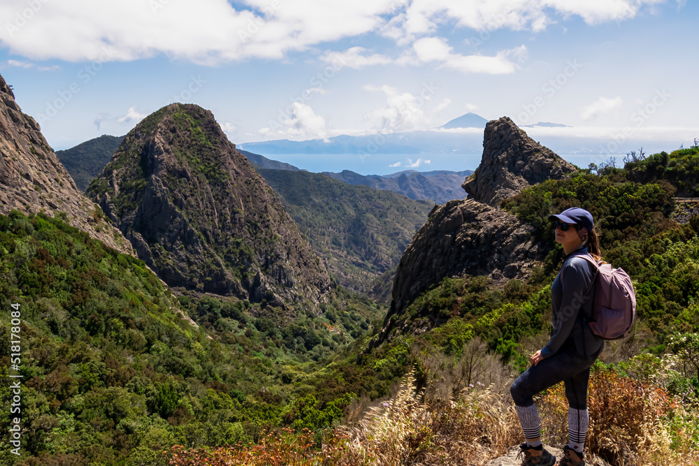 Woman with backpack watching volcanic rock formations in Garajonay National Park seen from Roque de Agando, La Gomera, Canary Islands, Spain, Europe. Hiking trail covered by forest and tropical fauna