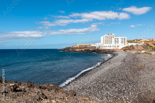 Panoramic view on a pebble stone beach Playa de San Blas near Los Abrigos, Tenerife, Canary Islands, Spain, Europe, EU. Coastline of the Atlantic Ocean. Big white vacation resort Santa Barbara