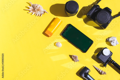 Two cameras, seashells, sunblock and a smartphone on a yellow background.