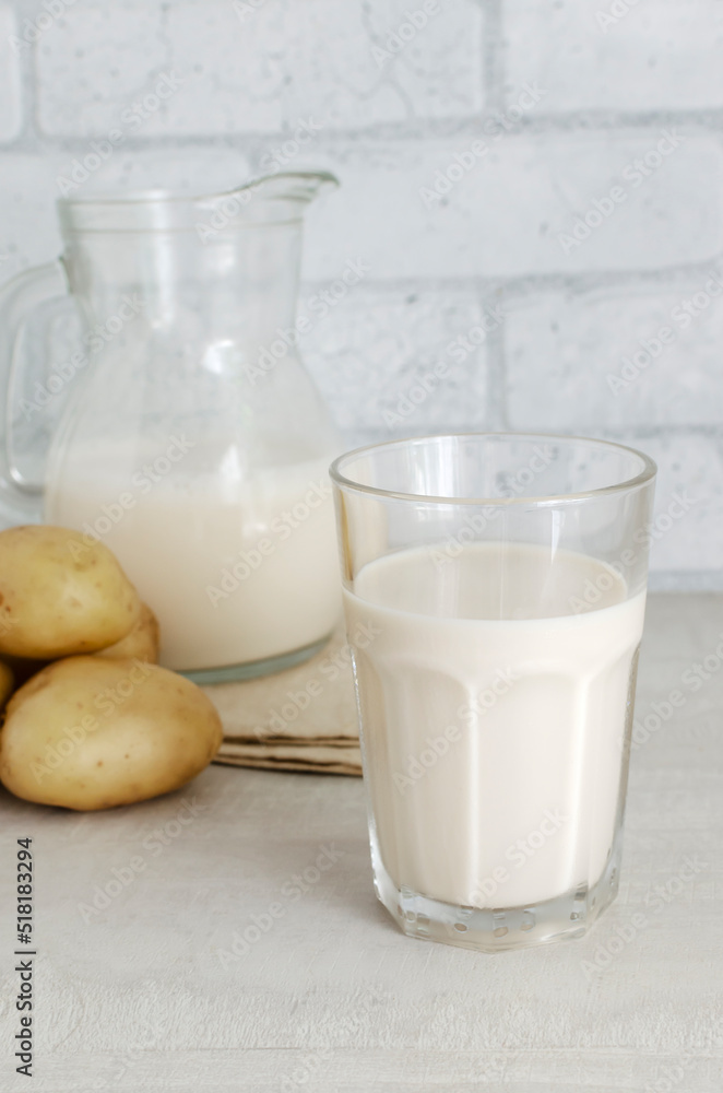 A transparent glass and a jug with potato milk on the table. A new trend in eating healthy. Alternative food concept. Vegetable Milk for Vegans. Vertical orientation. Selective focus A transparent glass and a jug with potato milk on the table. A new trend in eating healthy. Alternative food concept. Vegetable Milk for Vegans. Vertical orientation. Selective focus