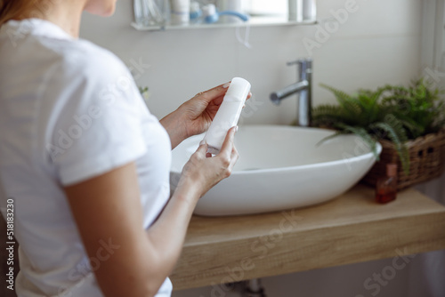 Rear of Caucasian woman holding cream or beauty product in bathroom. Over shoulder. 