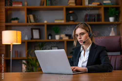 Attractive freelancer female talking in a video conference on line with a headset with microphone and laptop in an office desktop or home desk