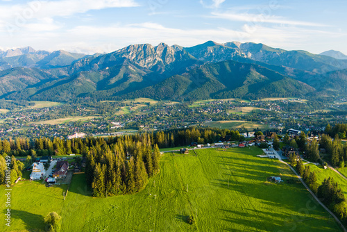 Fototapeta Naklejka Na Ścianę i Meble -  Aerial view of Zakopane town underneath Tatra Mountains taken from the Gubalowka mountain range. High mountains and green hills in summer or spring.