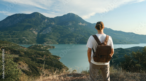 Back view of wanderlust man with backpack looking at scenic view of lake and mountains from a view point. photo