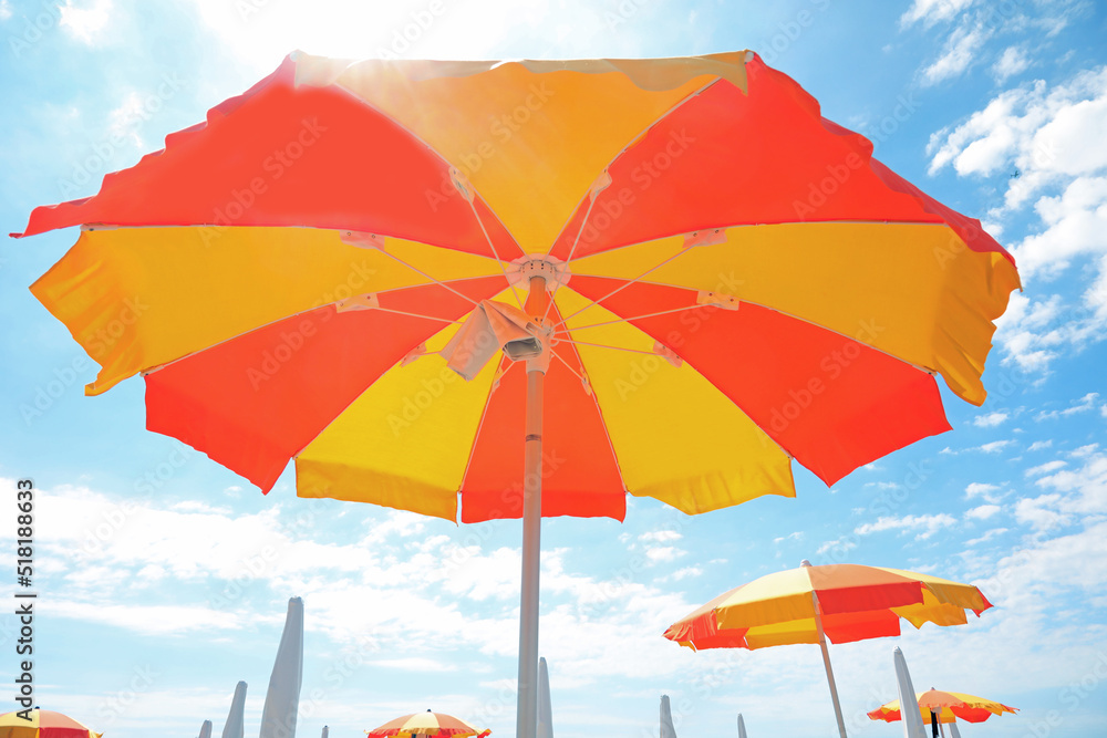 under a large yellow and orange umbrella on the sunny beach