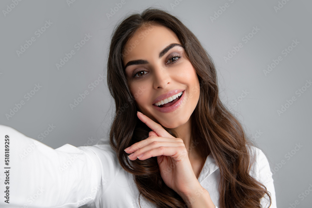 Photo of beautiful brunette woman laughing and taking selfie photo on cellphone isolated over gray background. Photo of beautiful brunette woman laughing and taking selfie photo on cellphone isolated over gray background.