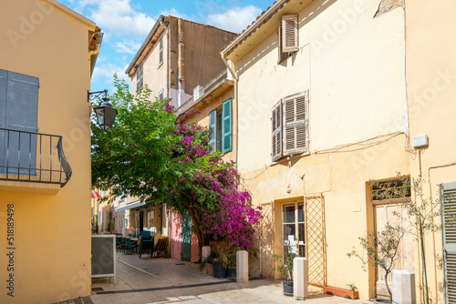 A picturesque alley with purple Bougainvillea flowers covering the entry and a sidewalk cafe with tables in the old town village section of Saint-Tropez, France, on the French Riviera. © Kirk Fisher