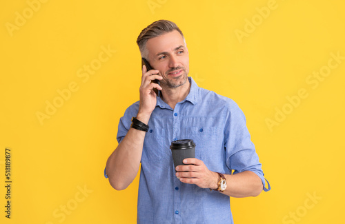 smiling mature man speaking on phone with coffee cup on yellow background, morning