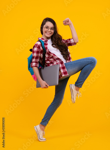 Back to school. Teenager schoolgirl hold notebook laptop. School children on isolated yellow studio background. Run and jump, jumping kid.