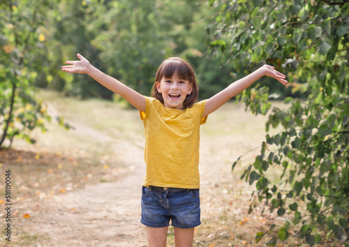 Young child arms raised up to sky, celebrating freedom. Positive children emotions. Free smiling girl in summer forest enjoying nature. Happy life concept