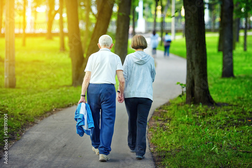 Elderly couple holding hands while walking together outdoors. Senior couple walking outdoors at park at summer sunny day, active lifestyle. Senior couple holding hands while walking on fresh air.