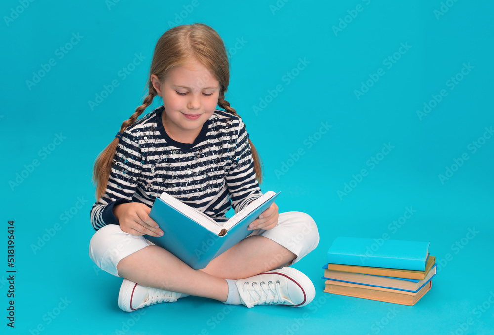 Child reading book sitting with legs crossed on blue background.
Child reading book sitting with legs crossed on blue background.