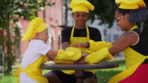Teambuilding of multinational children cooks in chefs hat and yellow apron uniform put hands on each other, having fun and laughing. Multiethnic kids commutication activity. photo