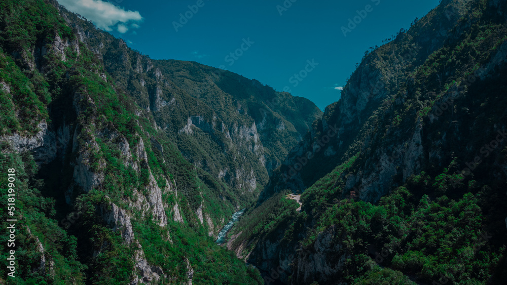 Obraz premium Narrow gorge of Piva river canyon close to the high road bridge over the valley. Green vertical rock formations and blue sky in the background, close to durmitor and Mratinje hydroelectric dam.