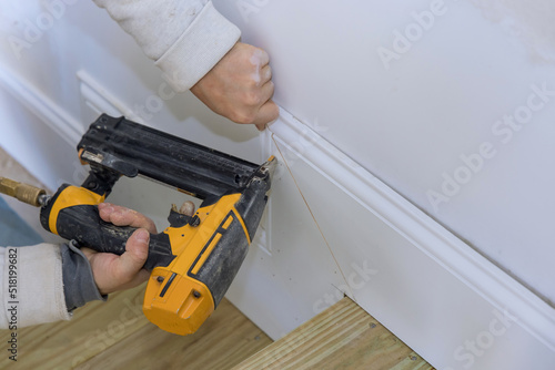 The carpenter uses a brad nail gun for the purpose of nailing the base molding trim on his new home © ungvar