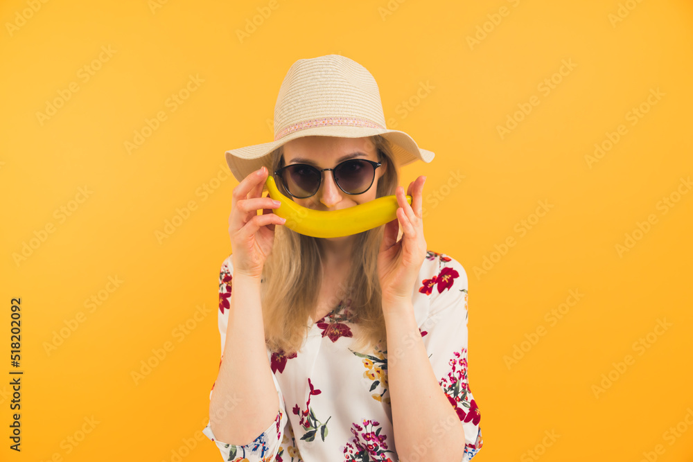 Time For Summer Holidays. Funny Banana Concept. Caucasian woman in her 20s in summer clothing holding a banana in front of her face. Smile concept. Orange background. High quality photo