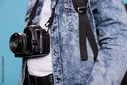 Close up shot of photography enthusiast having professional DSLR camera while standing on blue background. Photographer wearing denim jacket and having modern photo device