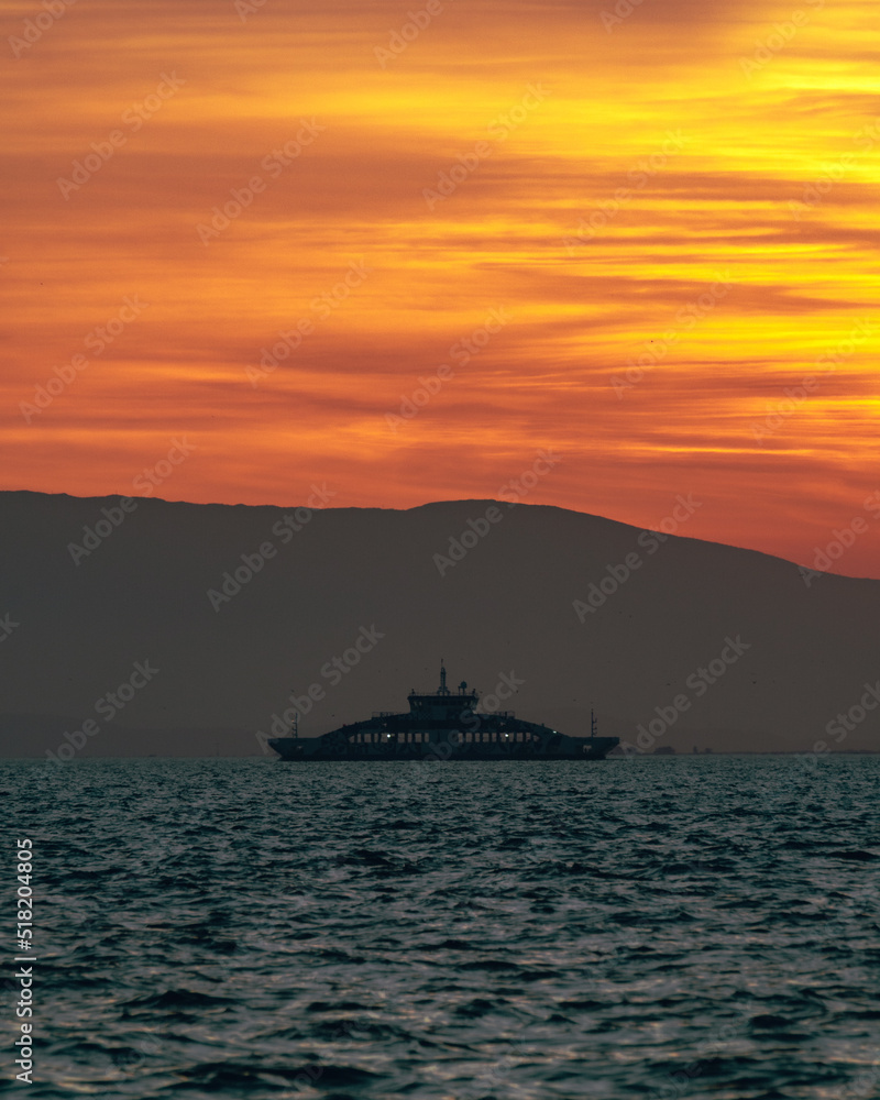 A silhouette of a ship in the sea with orange cloudy sky in the background.