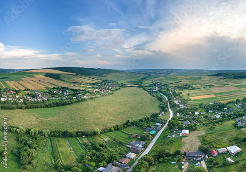 Fototapeta Naklejka Na Ścianę i Meble -  Aerial landscape view of village houses and distant green cultivated agricultural fields with growing crops on bright summer day