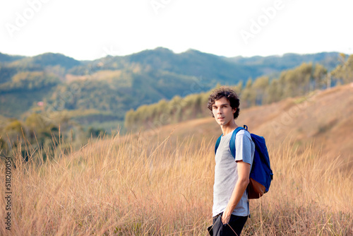 Person walking in the mountains. Man with curly hair looking at camera with mountains landscape in background.