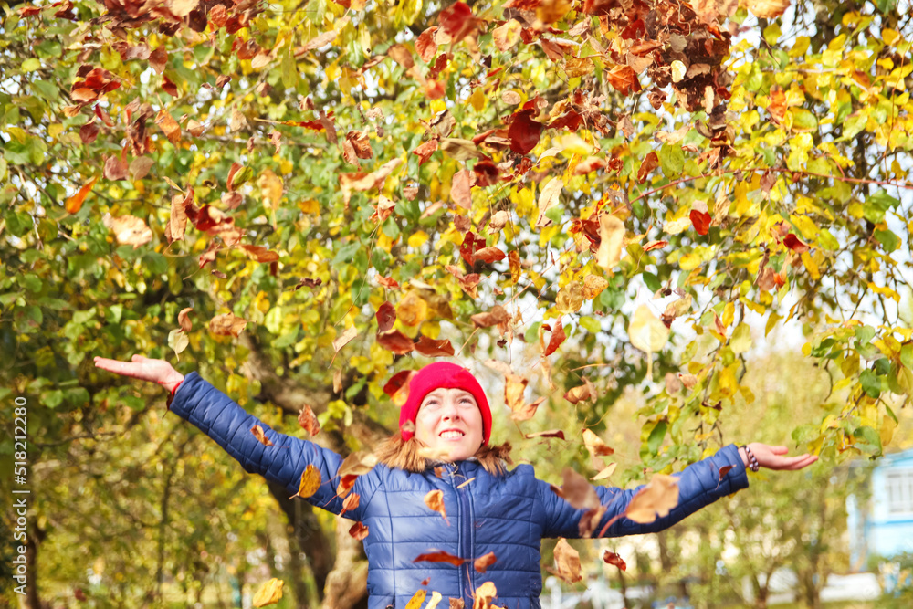 Defocus autumn people. Teen girl raising hand and throwing leaves. Many flying orange, yellow, green dry leaves. Joy autumn. Happy fall. Out of focus Defocus autumn people. Teen girl raising hand and throwing leaves. Many flying orange, yellow, green dry leaves. Joy autumn. Happy fall. Out of focus